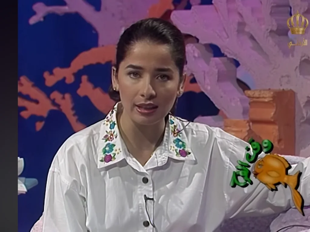 Aroub Soubh on Jordan Television in 1993, a white shirt with an embroidered collar, before the coral set of Waqt Al Farah, the goldfish and the programme's name beside her.