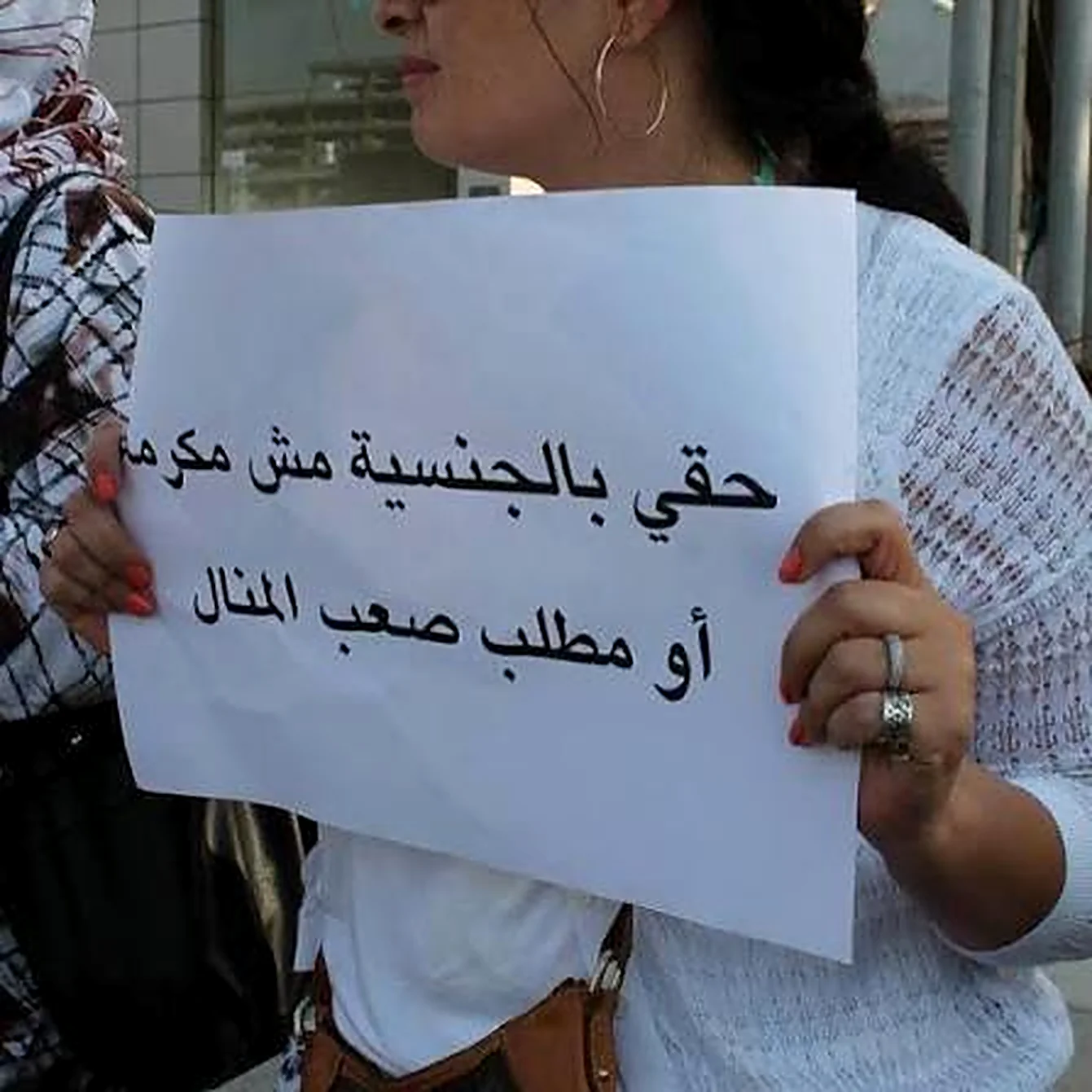 Aroub Soubh's hands holding a white sign at a demonstration, in Arabic: My right to nationality is not a favour, nor a demand beyond reach. Her photograph.