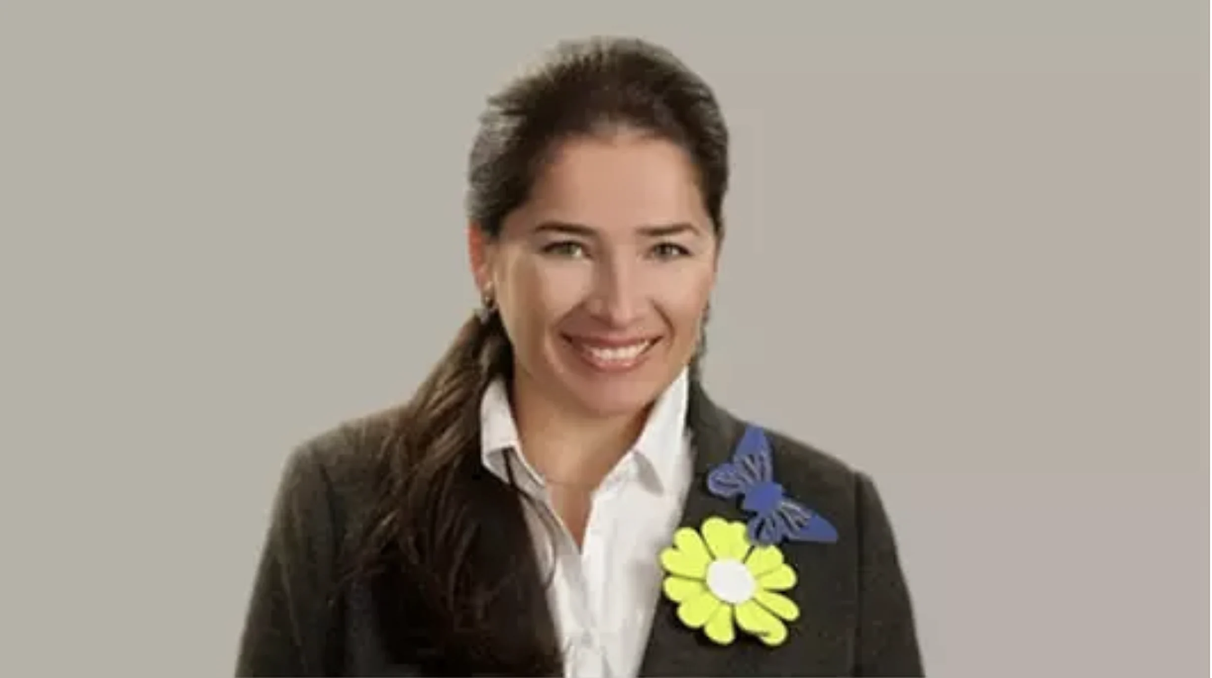 Aroub Soubh in a dark blazer with a yellow paper flower and a blue butterfly pinned to it, white shirt, smiling: her portrait on Monte Carlo Doualiya's site.
