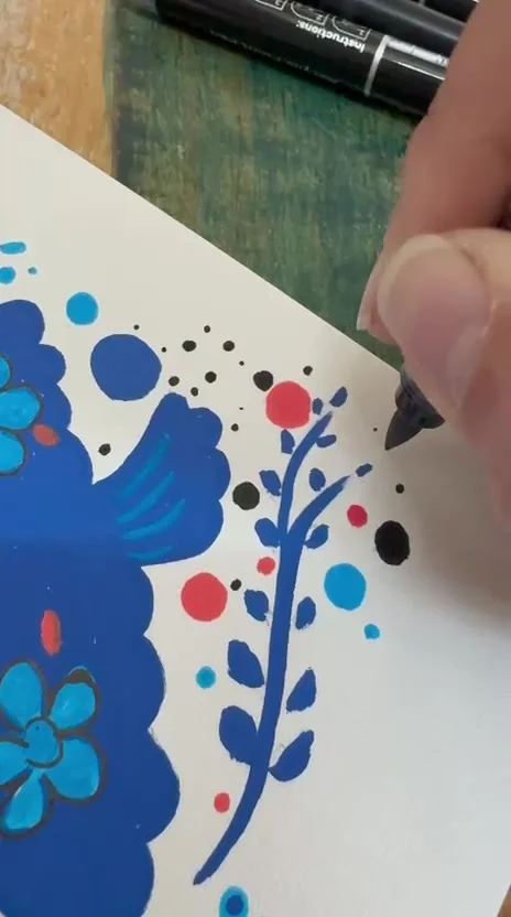 The same bird in cobalt marker on paper, a branch of blue leaves and red dots being added.